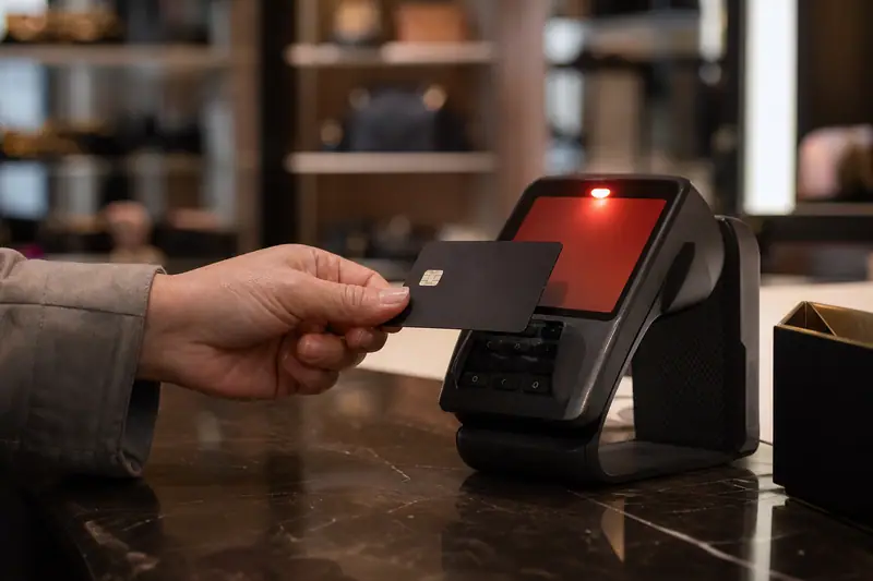 Main tenant une carte bancaire devant un terminal de paiement affichant un message d’échec, dans une boutique éclairée par une lumière naturelle