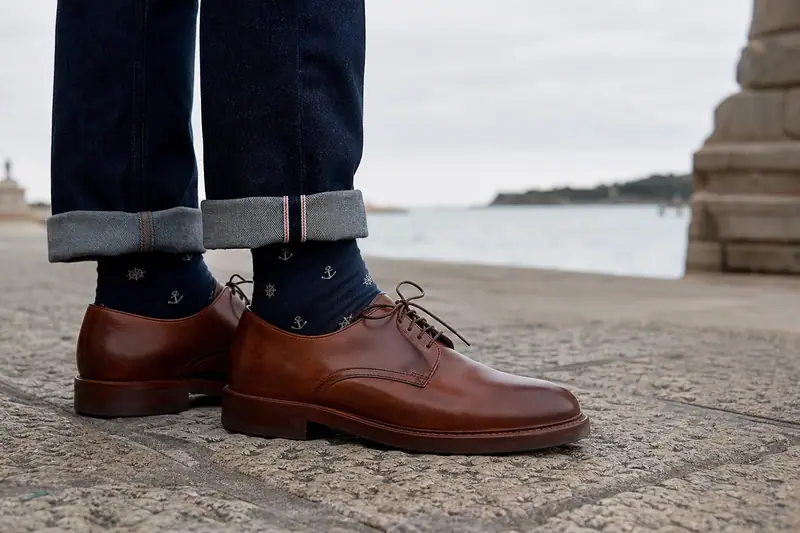 Chaussettes bleu marine à petits motifs marins portées avec un jean brut et des derbies marron