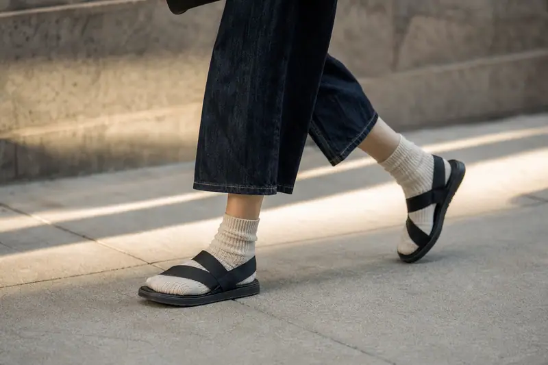 Paire de sandales noires à brides épaisses portée avec des chaussettes côtelées écrues