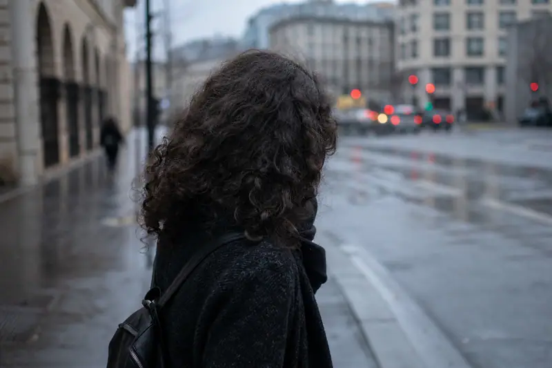 Femme marchant sous une pluie fine, cheveux gonflés et légèrement frisés par l’humidité ambiante