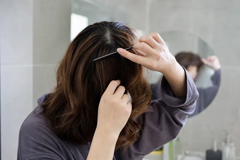 Personne se coiffant devant un miroir de salle de bain, racines des cheveux visibles