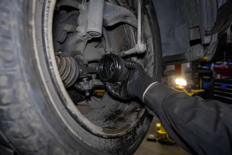 Main gantée d’un mécanicien tenant un soufflet de cardan derrière une roue avant, voiture levée en atelier