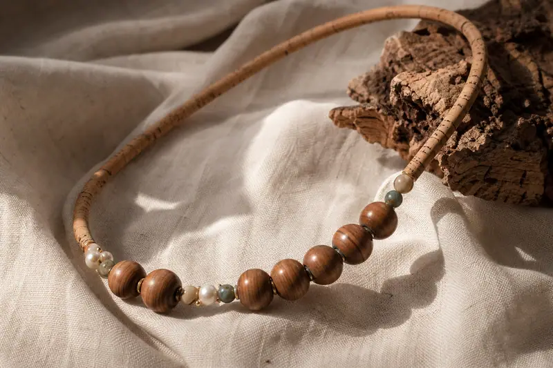 Collier artisanal en bois, cordon de liège et perles naturelles posé sur un textile en lin