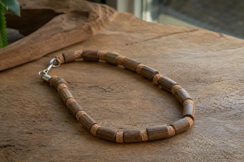 Collier artisanal en bois clair et liège posé sur une table en bois brut
