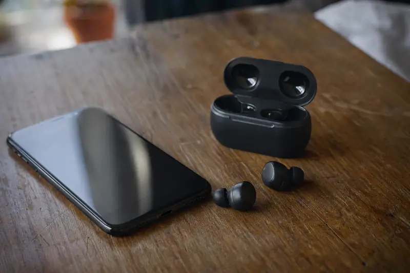 Écouteurs sans fil posés sur une table à côté d’un smartphone, boîtier de charge ouvert