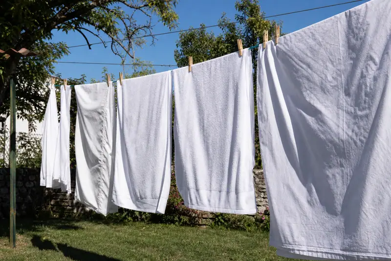 Draps et serviettes blancs suspendus à un fil à linge en extérieur sous le soleil