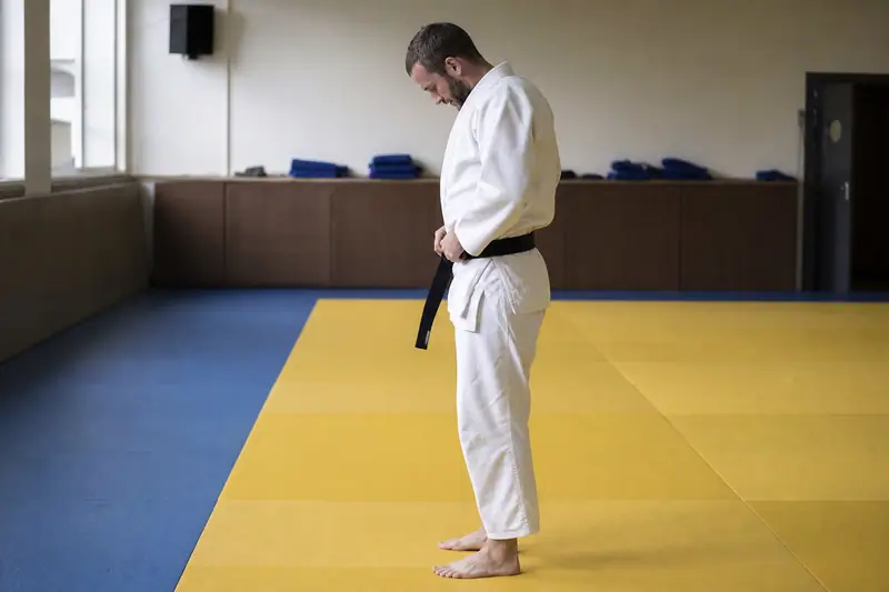 Judoka adulte ajustant la ceinture de son judogi blanc sur le bord d'un tatami