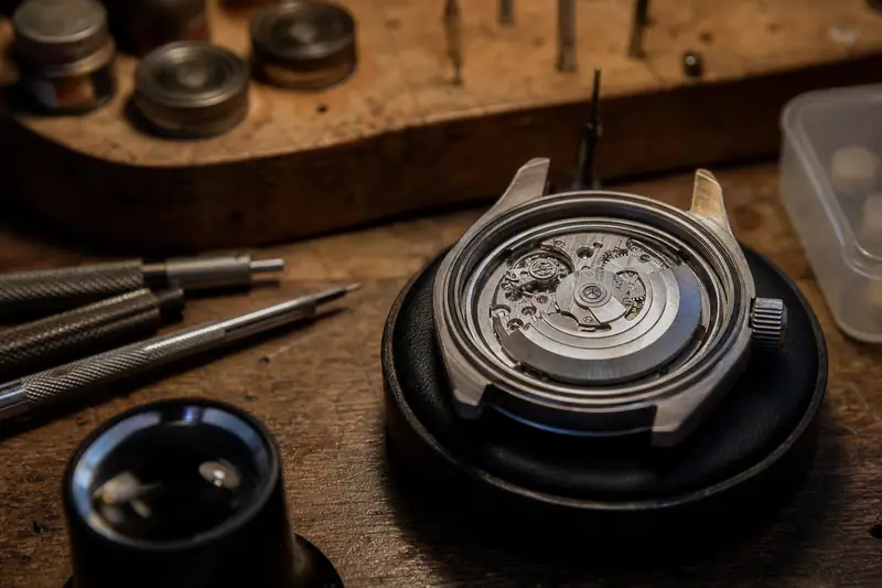 Montre automatique posée cadran ouvert sur l’établi d’un horloger, mécanisme visible