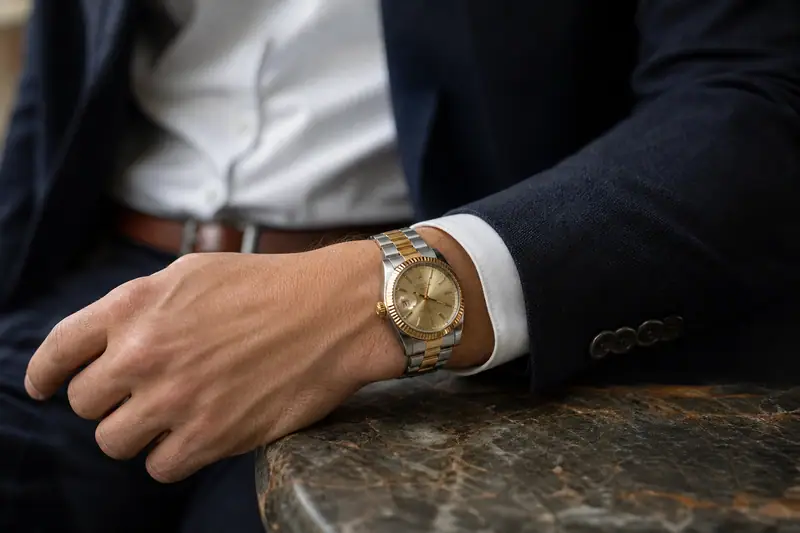 Montre bicolore acier et doré portée avec une chemise blanche et une veste bleu marine