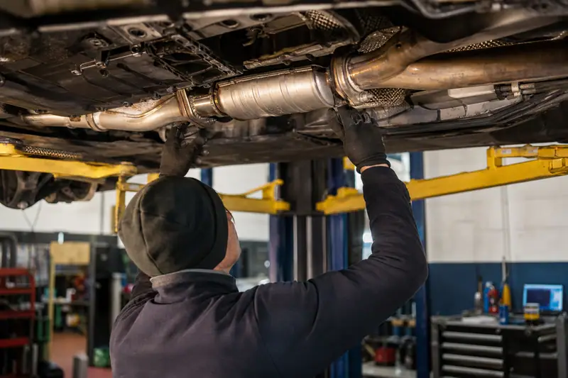 Mécanicien inspectant un catalyseur neuf et les raccords d’échappement sur une voiture levée