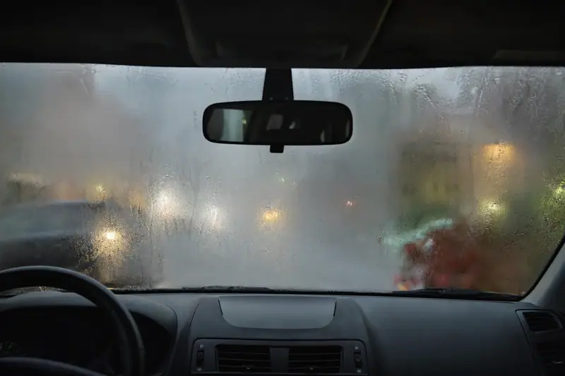 Pare-brise de voiture couvert de buée à l’intérieur, vue depuis le siège conducteur par temps pluvieux