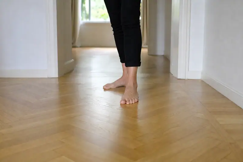Pieds nus sur un parquet en bois clair dans un couloir lumineux