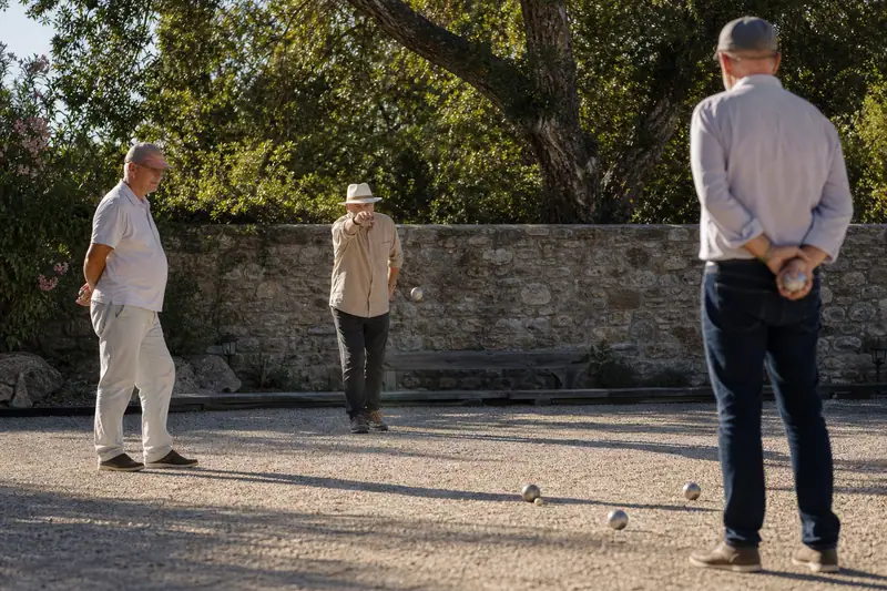 Joueurs de pétanque portant chaussures fermées et chapeaux sur un terrain de gravier
