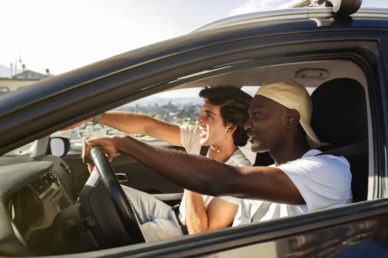 Deux voyageurs chargent leurs bagages dans une voiture avant un long trajet partagé