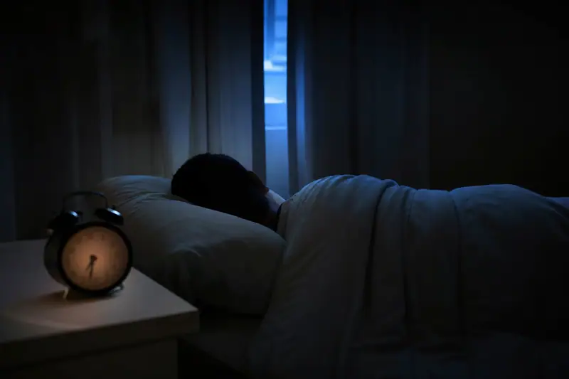 Personne allongée dans un lit, yeux ouverts dans la pénombre, réveil affichant une heure matinale posé sur la table de nuit