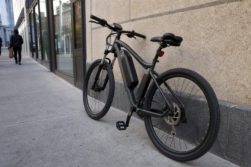 Vélo électrique garé contre un mur en ville, batterie visible sur le cadre, écran de contrôle allumé sur le guidon