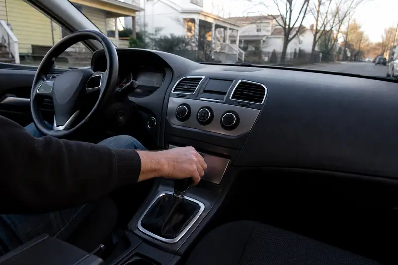 Conducteur au volant d’une voiture, main posée sur le levier de vitesses, moteur allumé