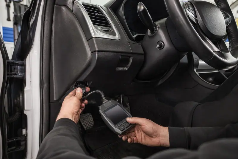 Mains d’un mécanicien branchant une valise de diagnostic électronique sous le tableau de bord d’une voiture, portière ouverte