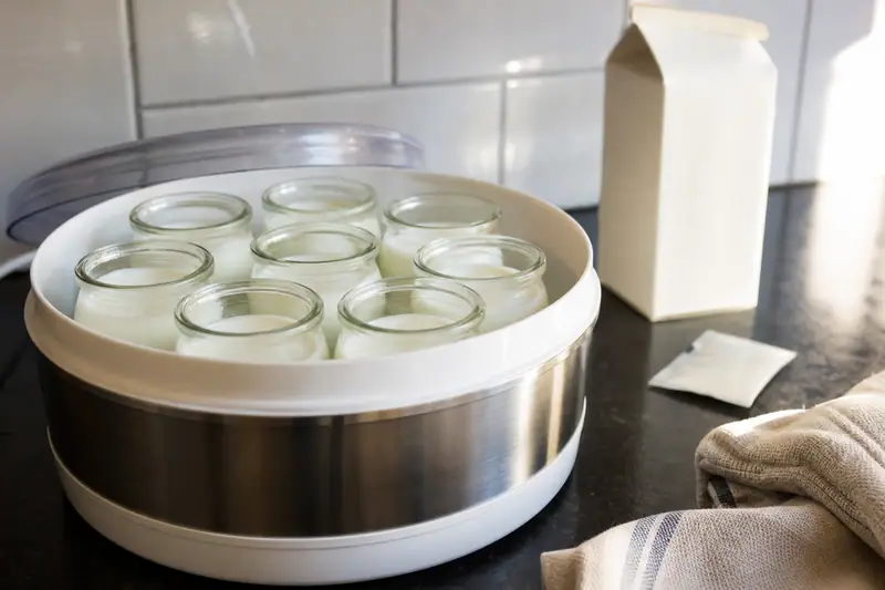 Pots de yaourt en verre dans une yaourtière ouverte sur un plan de travail de cuisine